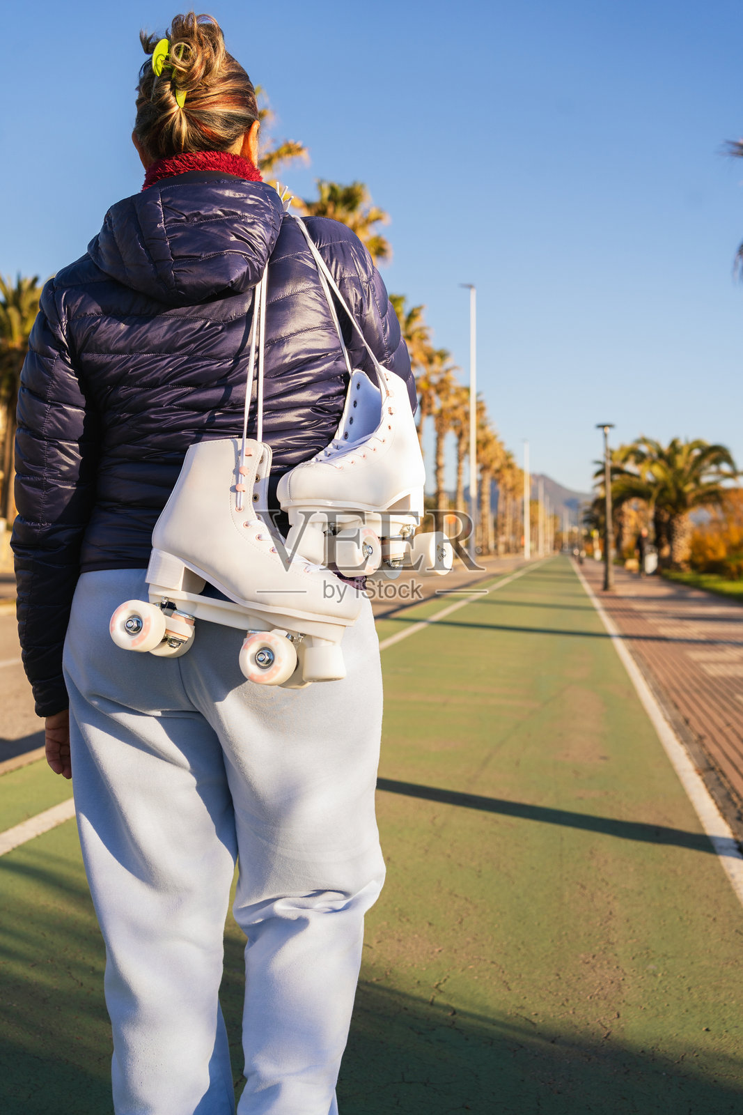 一位老年女性在公园里走开，手里提着滑轮溜冰鞋。照片摄影图片