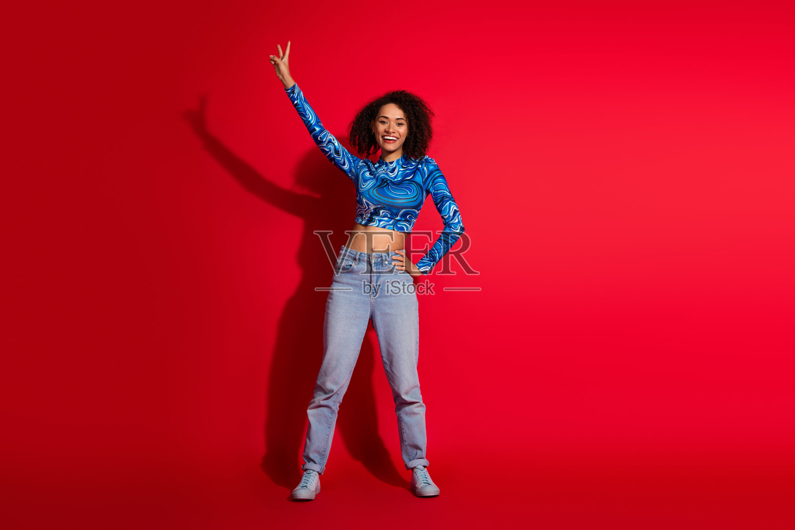 时尚的年轻女性穿着流行的蓝色图案上衣和休闲牛仔裤，做出和平手势。照片摄影图片