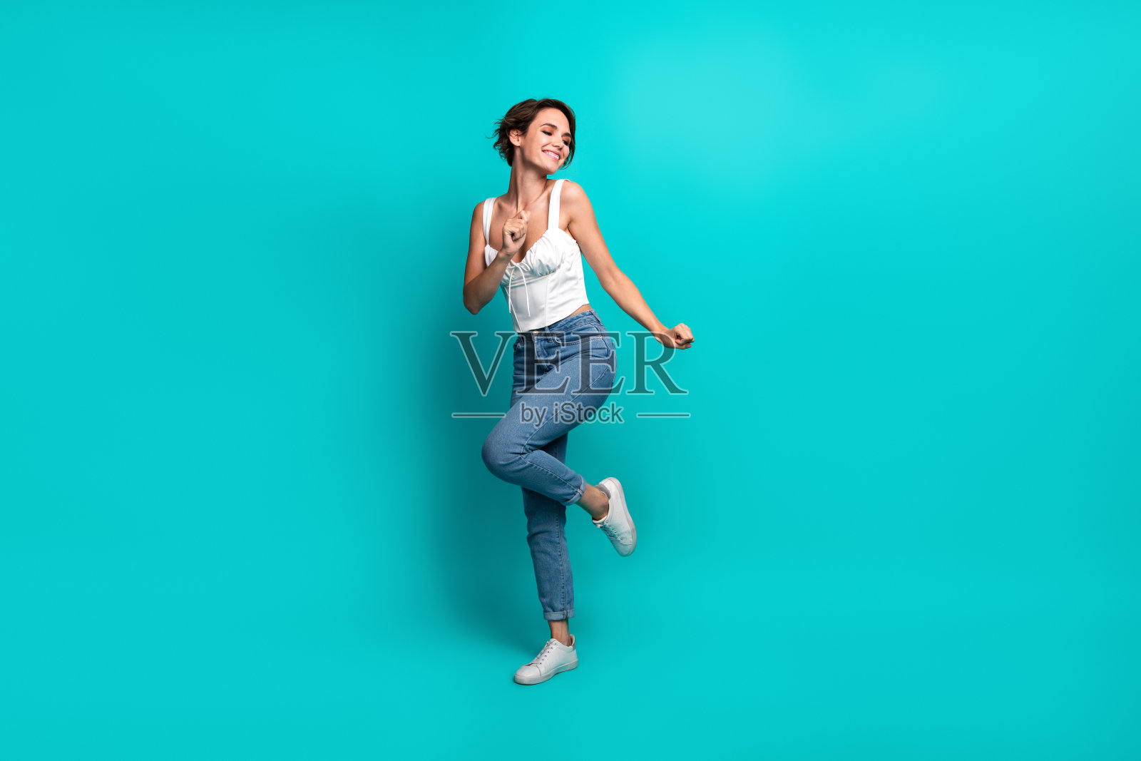 穿着时尚的快乐女性在充满活力的青绿色背景前摆姿势，展现积极的能量和活力照片摄影图片