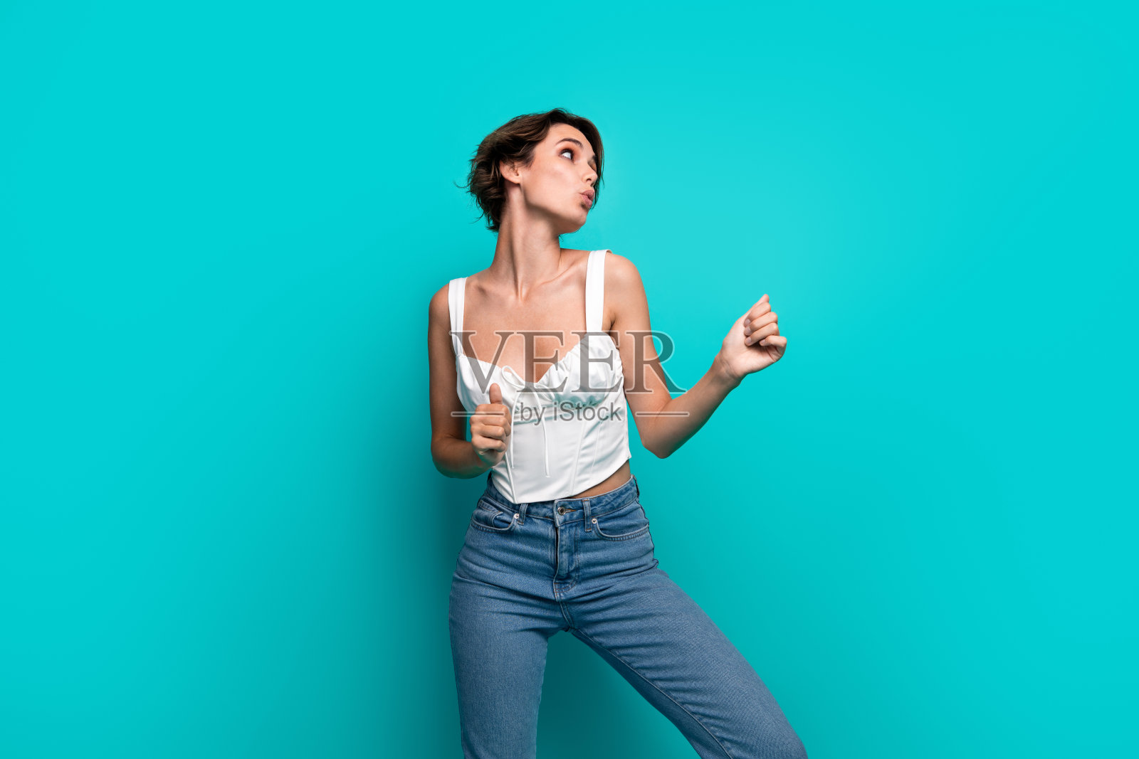 时尚的年轻女性，留着波波头，穿着时尚的白色上衣和牛仔裤，摆姿势于生动的青绿色背景前。照片摄影图片