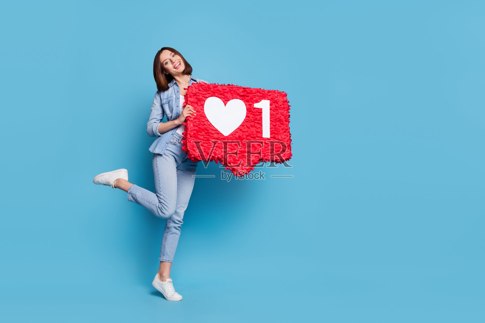 可爱的闪亮女性穿着牛仔衬衫，走路时手持皮纳塔，背景为蓝色的空白空间。照片摄影图片