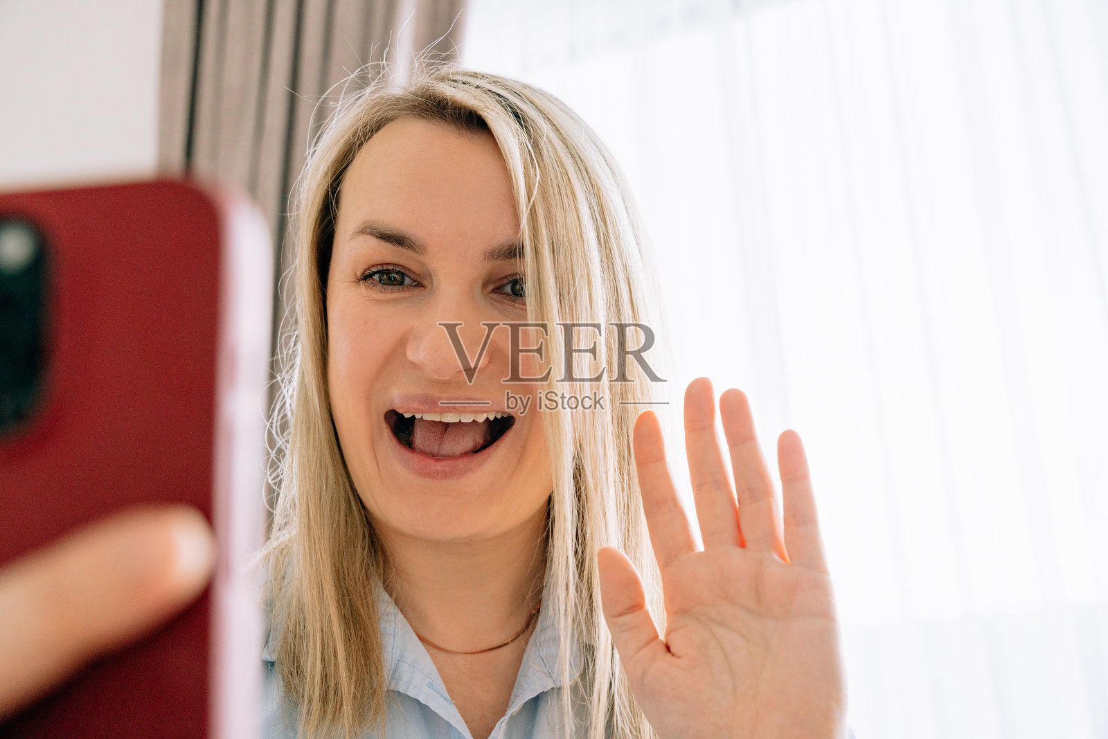 微笑的35-37岁欧洲外貌女孩特写，穿着蓝色衬衫，正在用手机视频通话。照片摄影图片