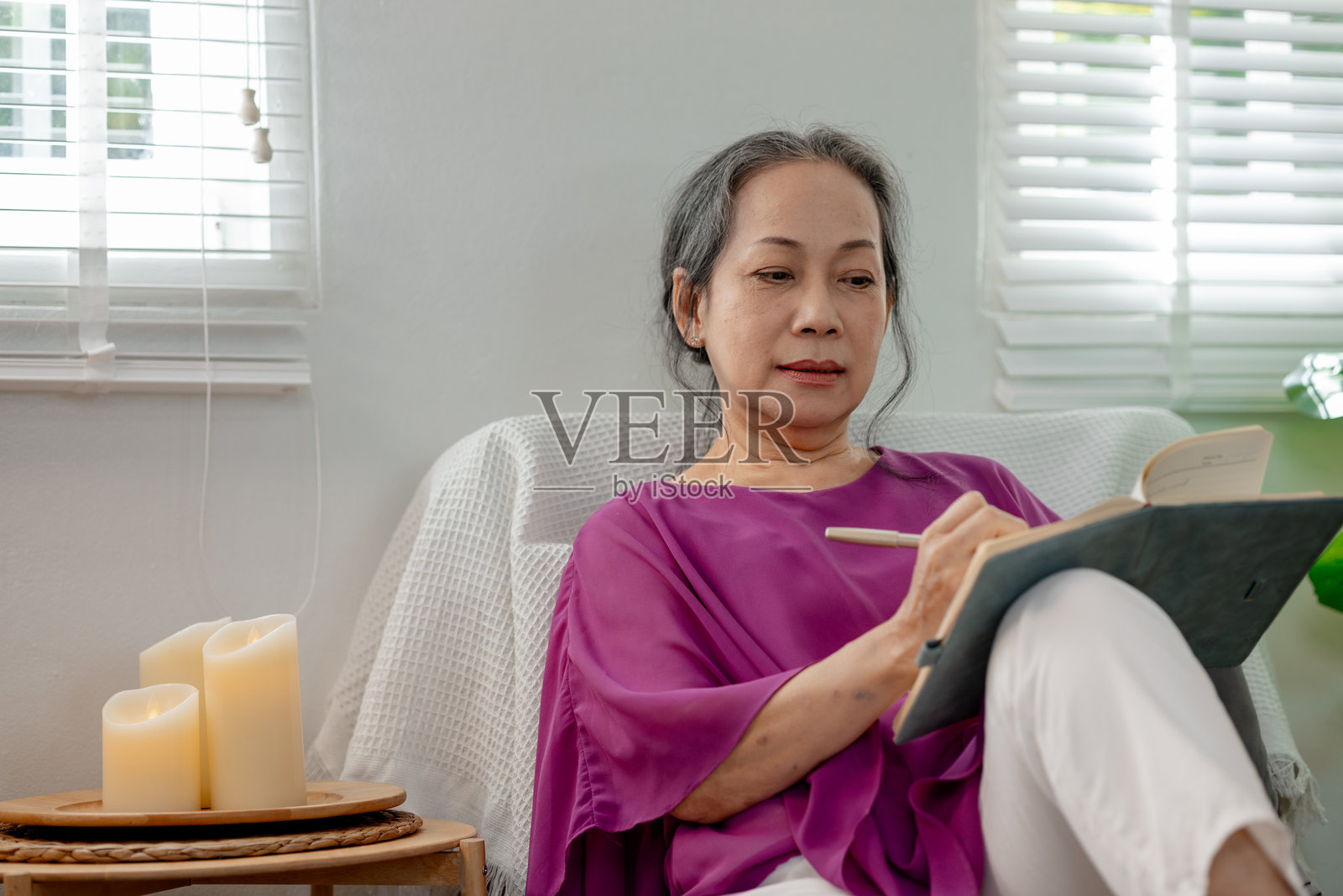 一位老年妇女在家中幸福地度过退休生活，一位善良的老妇人愉快地记录下她生活中发生的事件，因为那是一个值得回忆和美好的时光。照片摄影图片