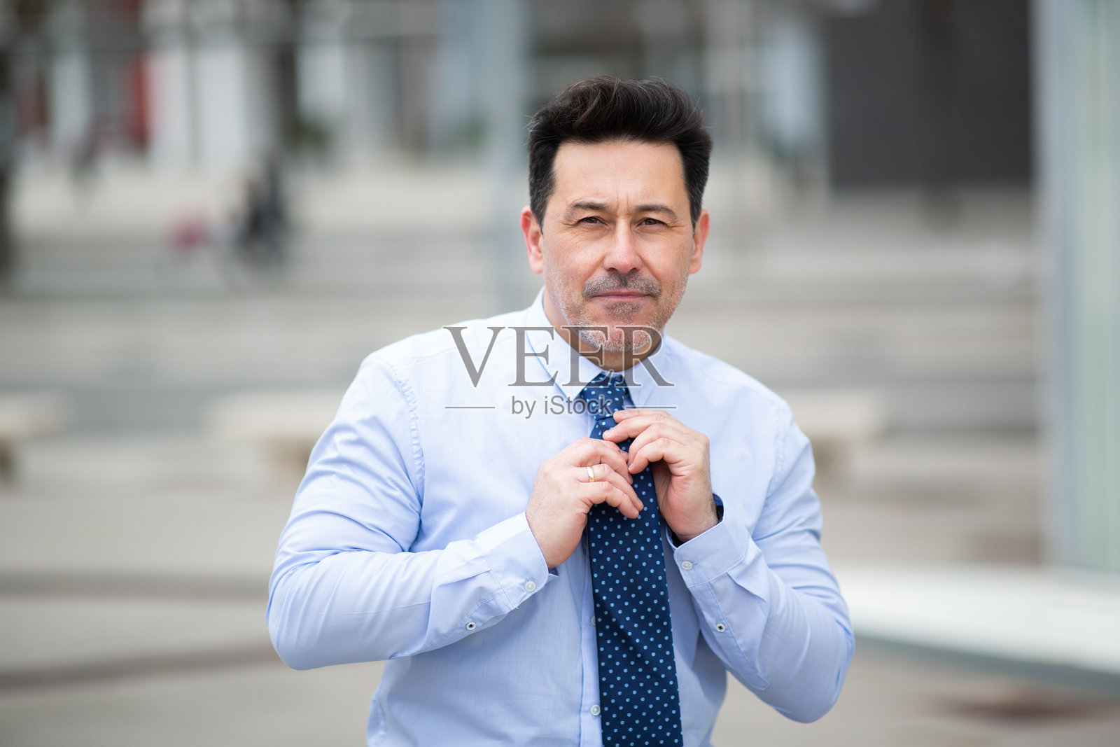 自信的成熟商人在外面调整他的领带照片摄影图片