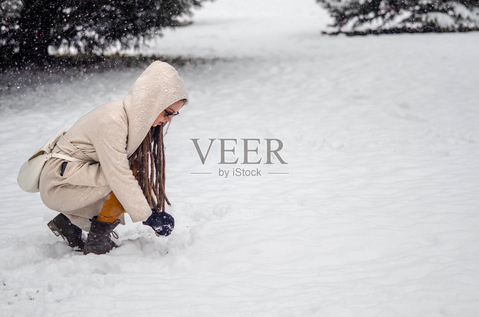 一位长着长辫子的年轻女性在冬季仙境中尽情享受，雪花轻轻覆盖在她身上，她正在捏一个雪球准备开始一场有趣的雪仗。照片摄影图片