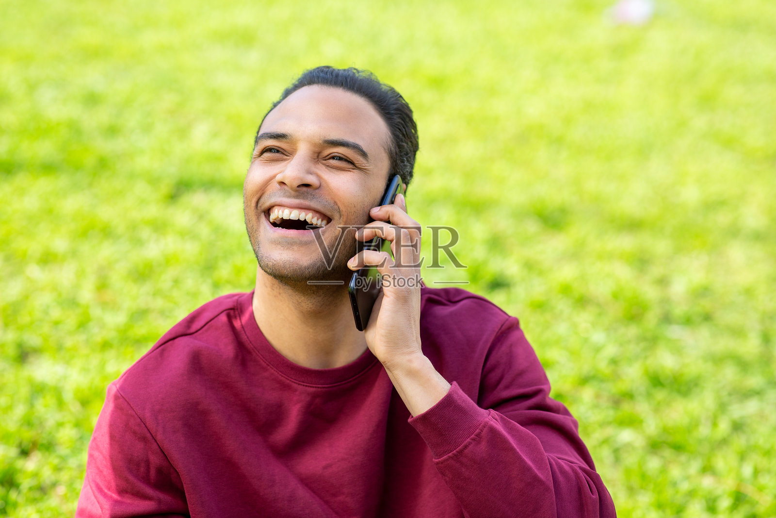 快乐的年轻黑人男子坐在公园里打手机。照片摄影图片