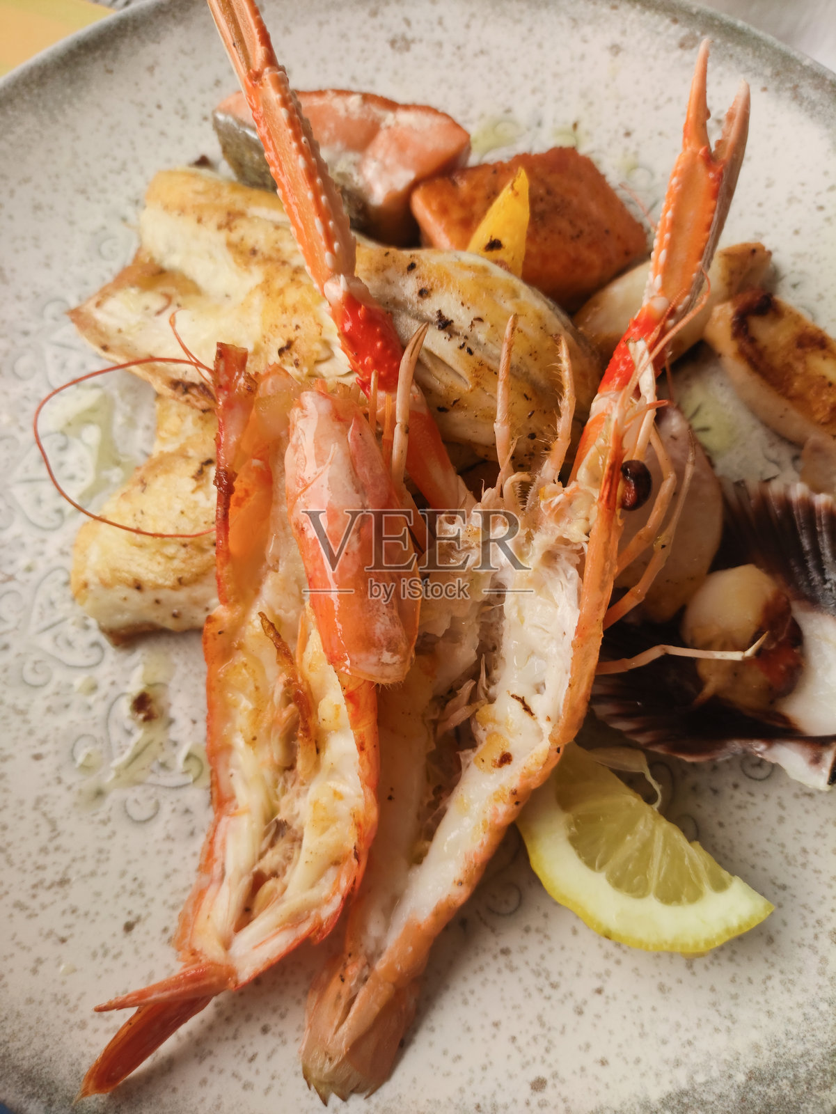 乡村风格的盘子上摆放着烤海鲜拼盘，突显多汁的虾、鲜嫩的鱼和带有地中海风味的酸爽柠檬角。照片摄影图片