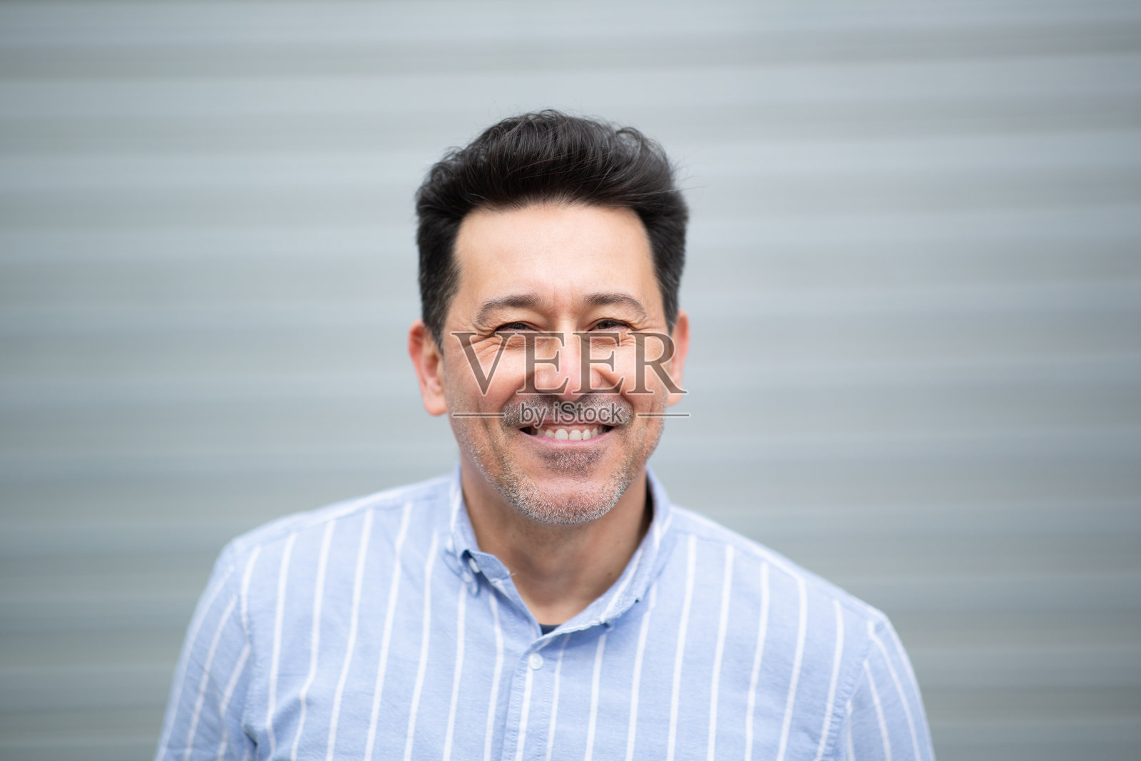 微笑的成熟拉丁裔男性站在灰色背景前照片摄影图片