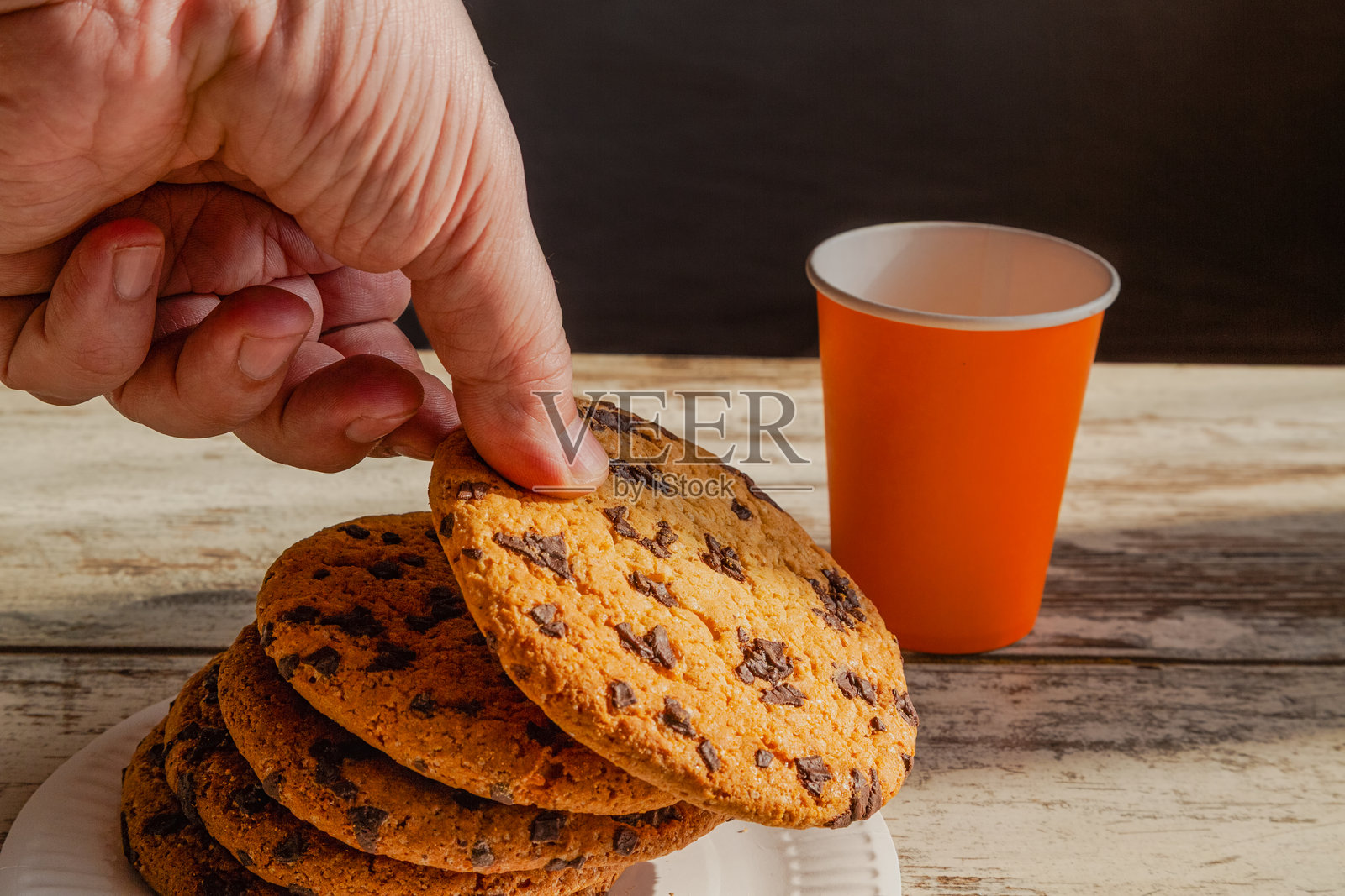 手中拿着一块饼干象征着丰盛、热量丰富的小吃和快速的早餐。桌子上放着一个一次性盘子，上面有饼干，一只手正伸向其中一块饼干。照片摄影图片
