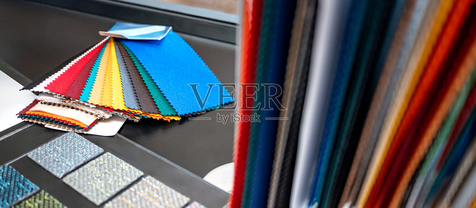 一组色彩丰富的面料样本。桌上有各种颜色和纹理的面料片以及地毯样本。照片摄影图片