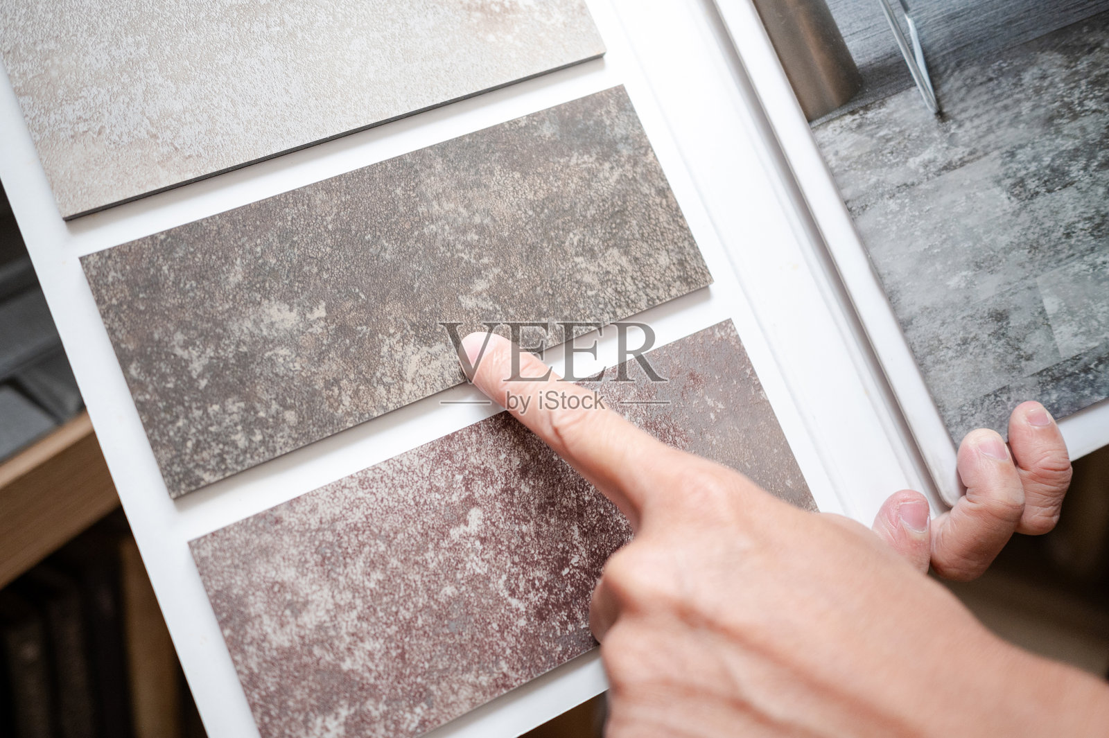 地板材料设计系列。设计师手指着展示目录中的石材瓷砖样本。顾客在家居设计商店选择粗糙的纹理和图案作为地面装饰。照片摄影图片