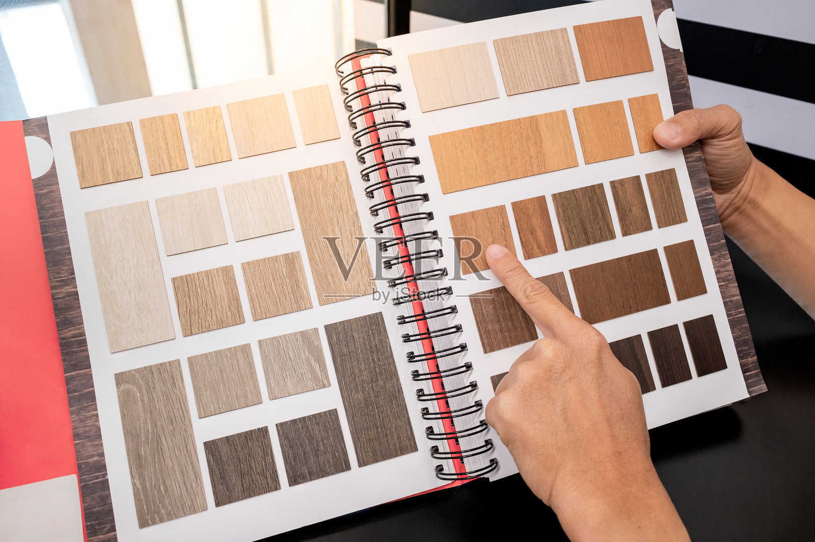 设计师手指着材料样本目录中的木质层压板样本集合。客户正在为家具饰面或室内建筑设计选择自然木纹。照片摄影图片