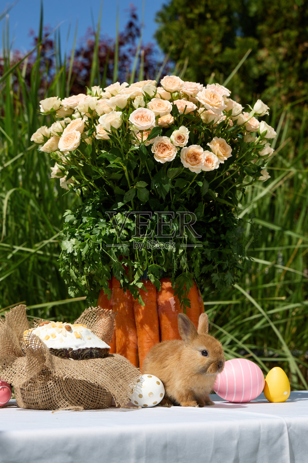 年轻的小兔子在篮子里，旁边有复活节彩蛋、蛋糕和花朵，置身于户外。照片摄影图片