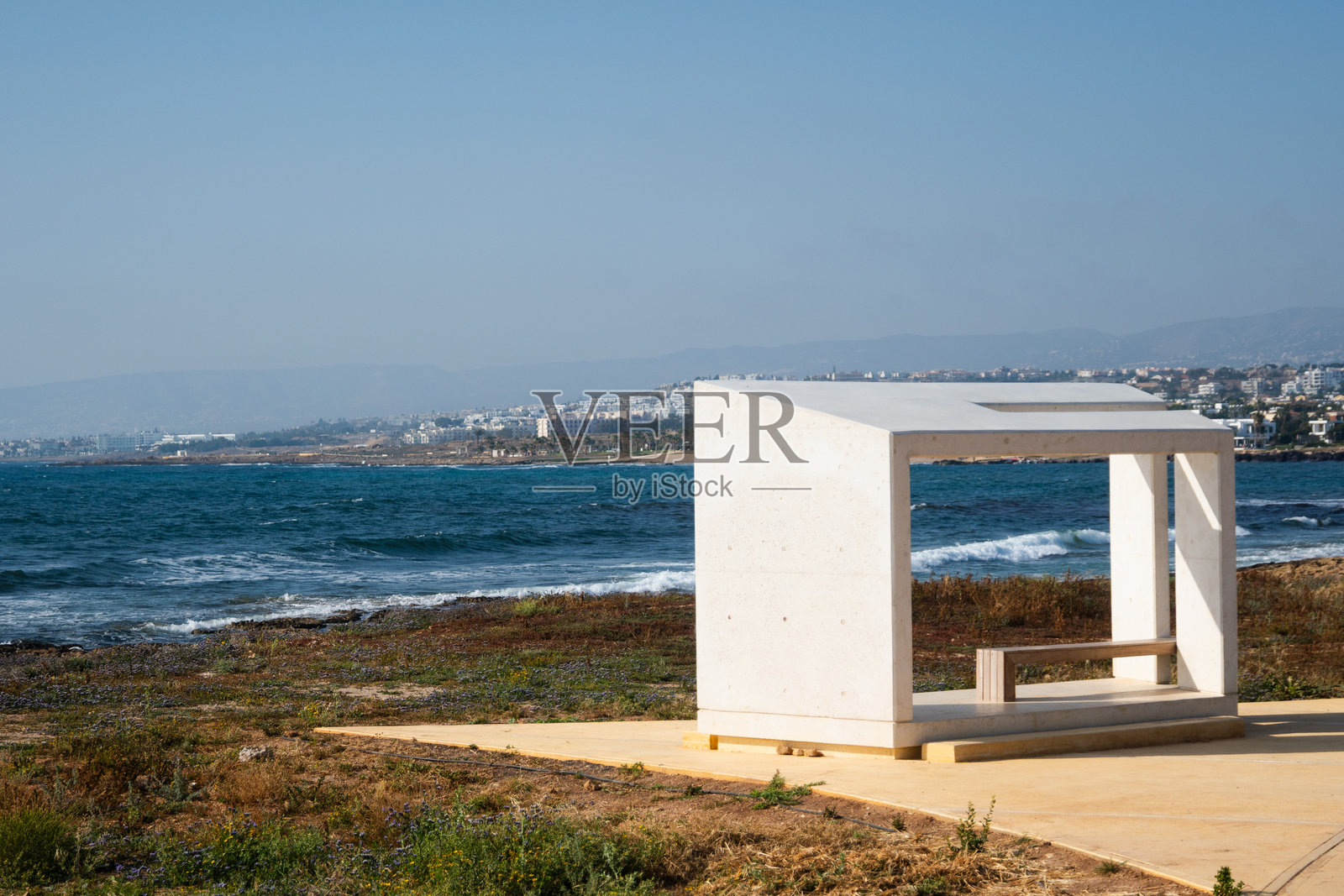 塞浦路斯帕福斯海滨。一个立方体的白色长椅，现代建筑风格，背景是深蓝色的地中海。理想假期的概念，塞浦路斯和希腊的地中海风光。照片摄影图片