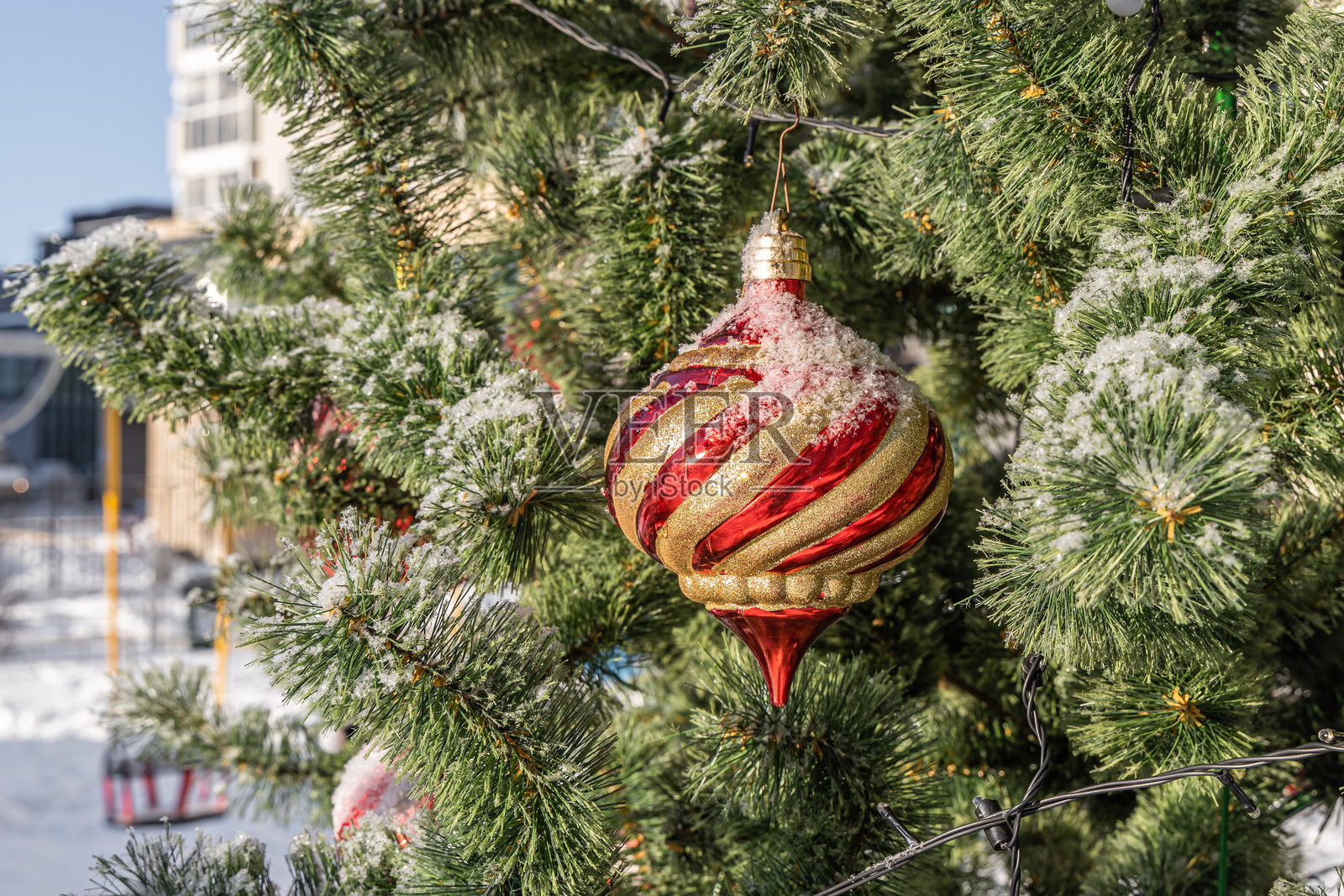 户外的绿色塑料圣诞树上挂着雪和红色玻璃球。圣诞装饰。照片摄影图片