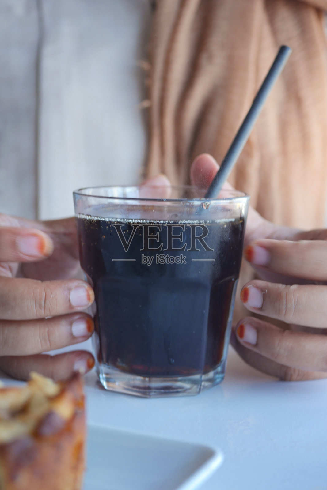 一只优雅的玻璃杯装满深色饮料，配有吸管和手握着它。照片摄影图片