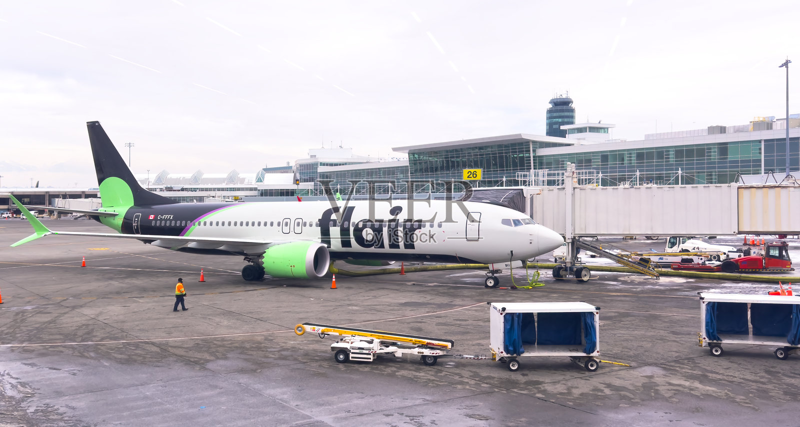 一架加拿大超低成本航空公司Flair Airlines的波音737停靠在机场登机口,连接着登机桥,地勤人员在旁。照片摄影图片