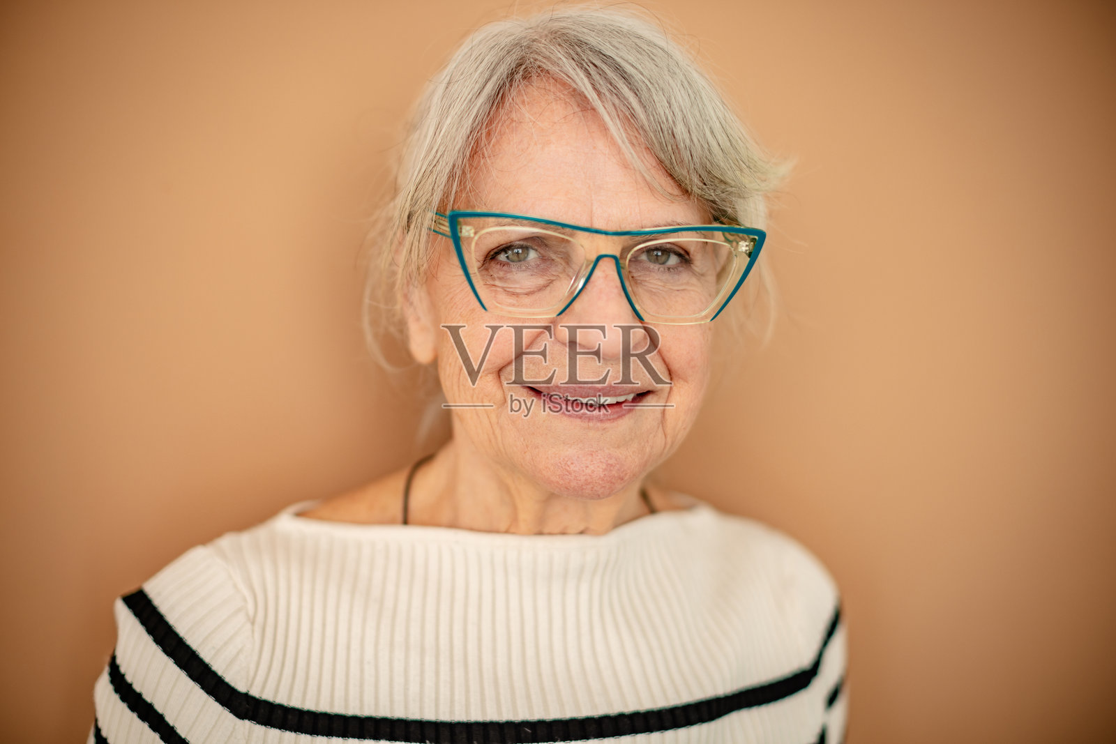 戴着现代眼镜的老年人微笑着，背景温暖。照片摄影图片