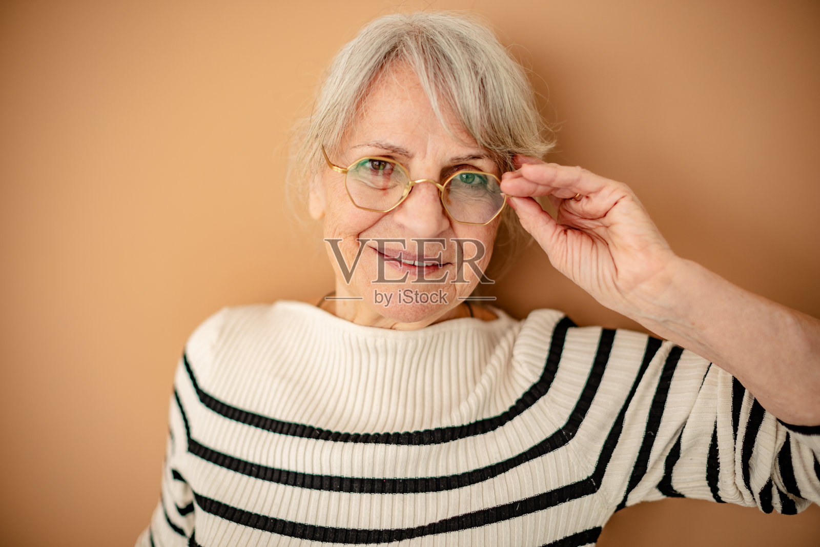 一位佩戴现代眼镜的老年人，在舒适的室内环境中自信地微笑。照片摄影图片