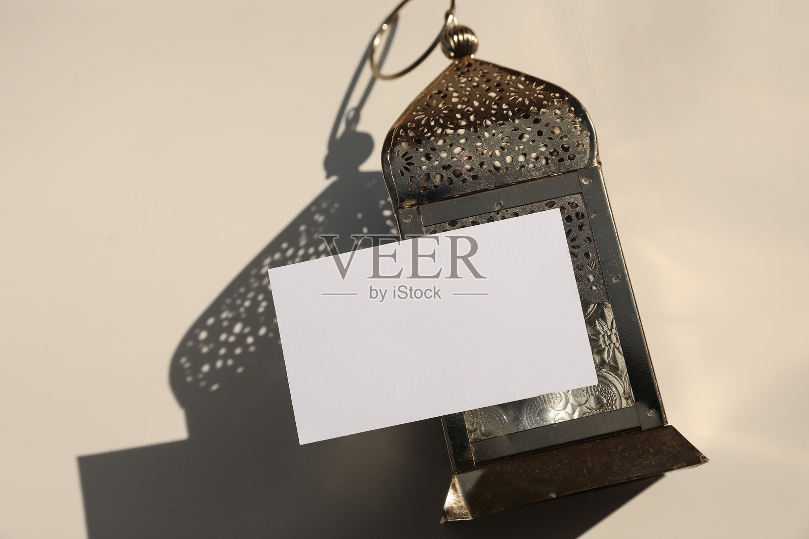 空白贺卡，邀请函模板在金色金属装饰摩洛哥灯笼上的展示。米色桌面背景，阴影，俯视图。节日横幅静物，穆斯林节日拉马丹快乐。开斋节快乐。照片摄影图片