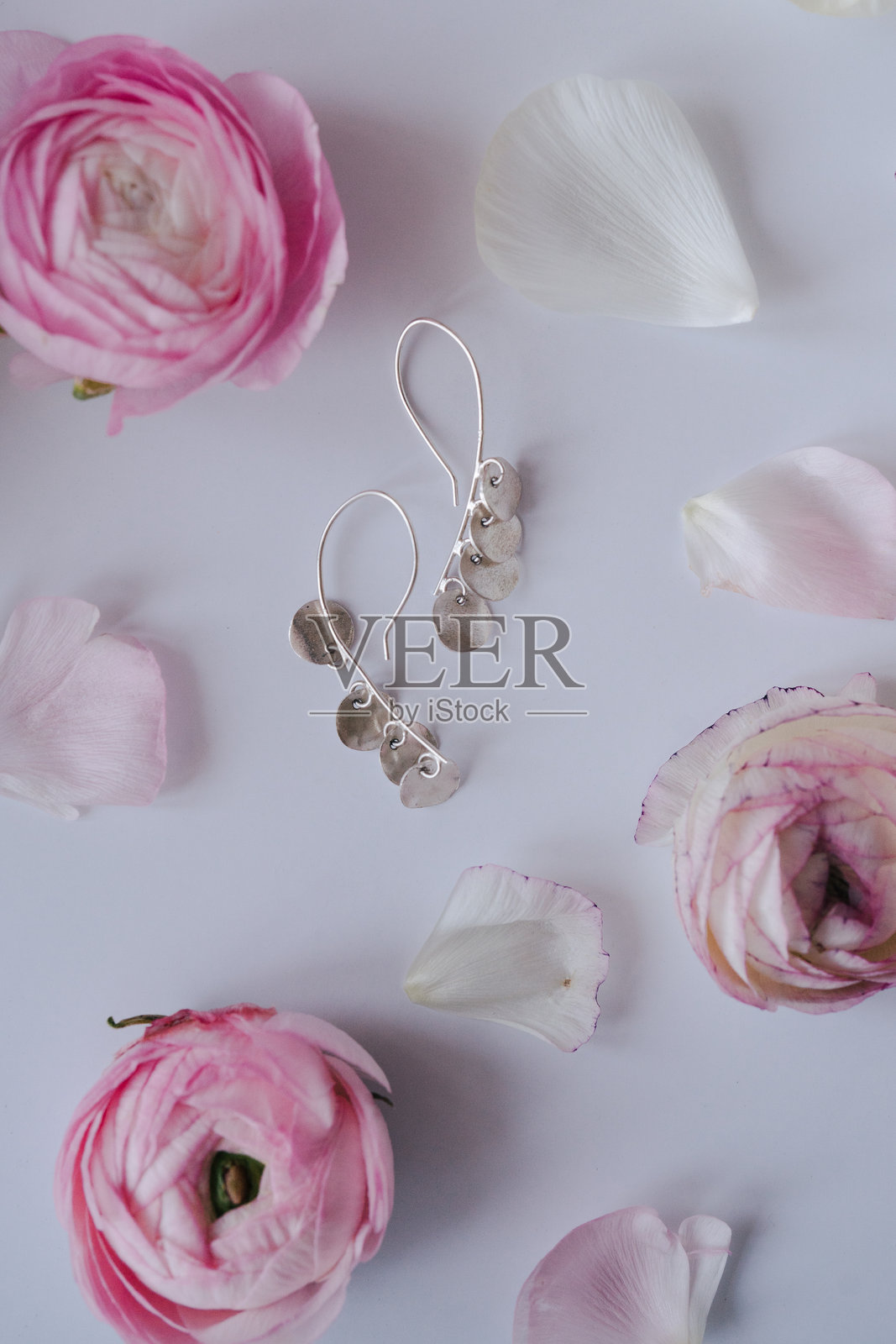 白色背景上的银色耳环和花朵。女性时尚精品品牌构图。优雅的女性珠宝。平铺，俯视图。照片摄影图片