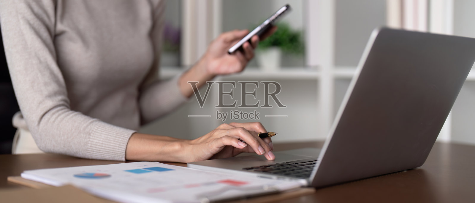 女性一边使用智能手机一边操作笔记本电脑，管理财务和在线活动。照片摄影图片