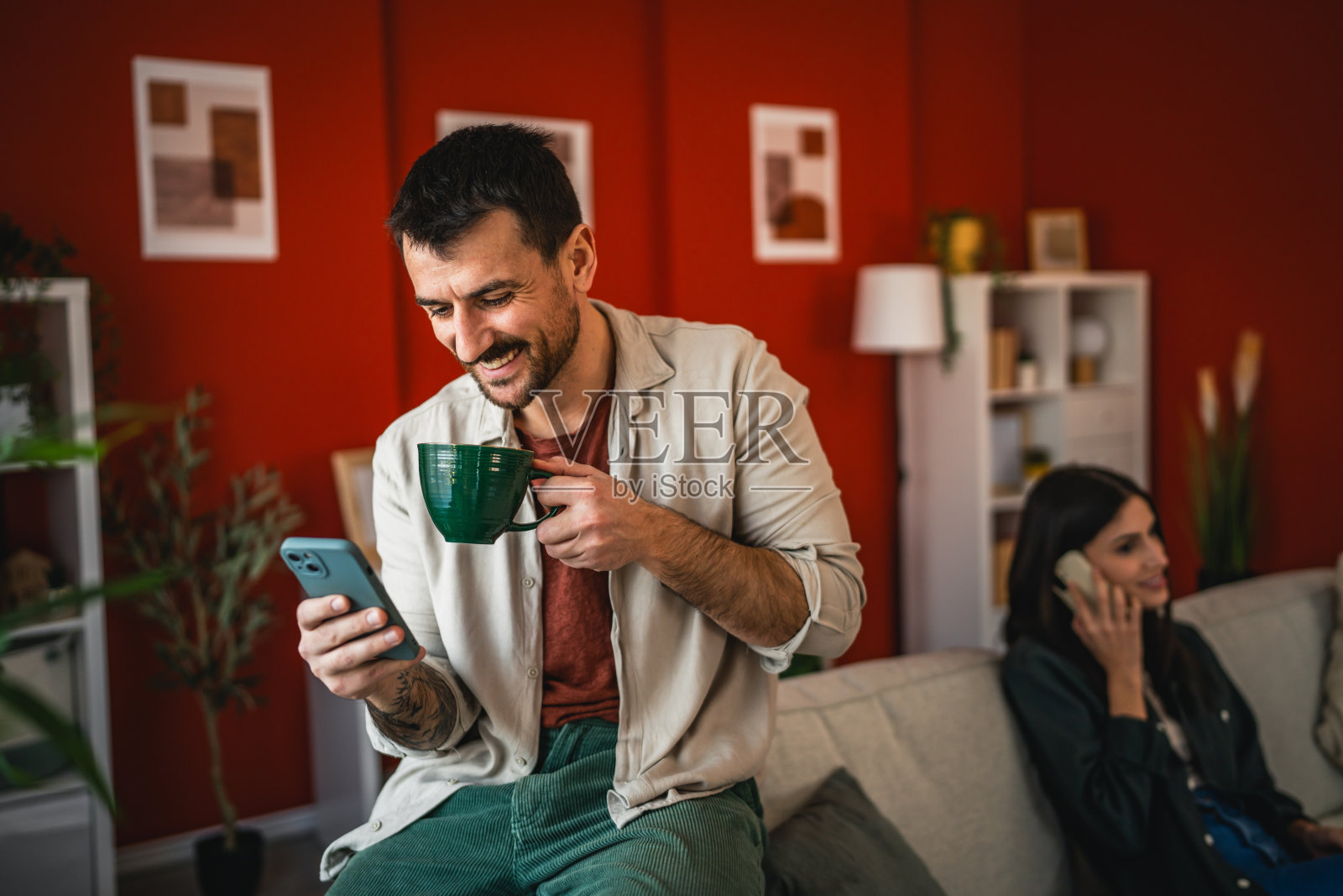 放松的男人坐在家里，使用手机并喝咖啡照片摄影图片