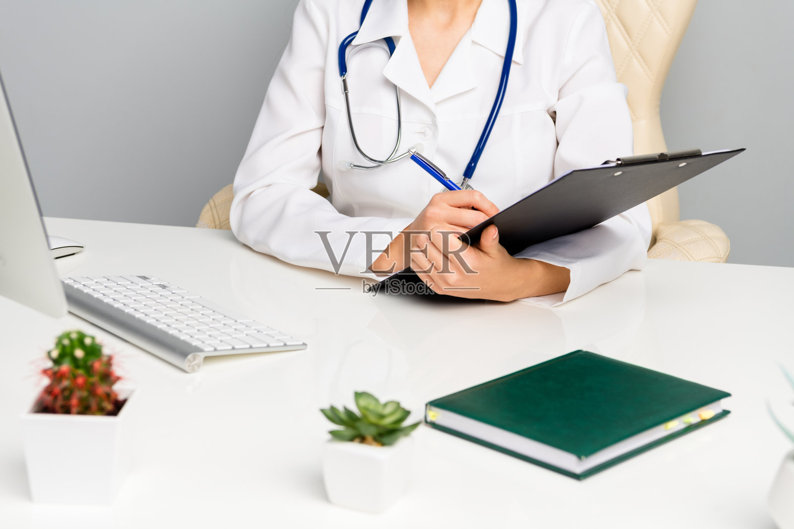 年轻女医生在医疗诊所的桌子旁，手持夹板和听诊器。照片摄影图片