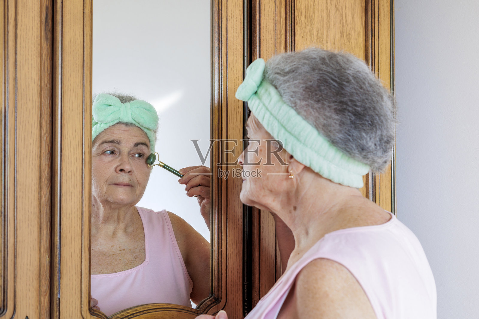 老年女性在家使用玉石滚轮进行面部按摩 - 抗衰老护肤程序。留白。照片摄影图片