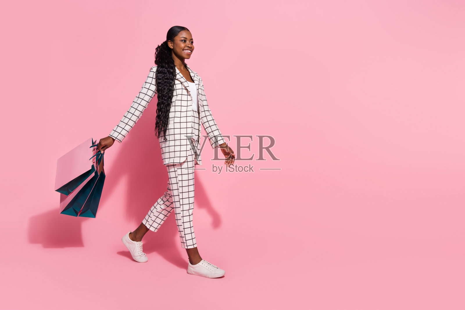 年轻漂亮女孩在购物中心的侧面全身照，空旷的折扣空间，背景为粉色。照片摄影图片