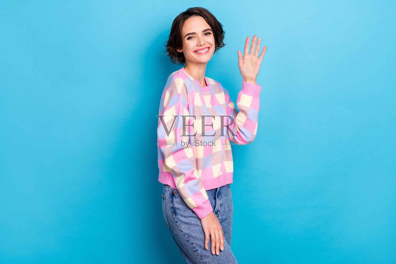 年轻漂亮的女孩侧面头像，心情愉快，向大家挥手，背景为蓝色。照片摄影图片