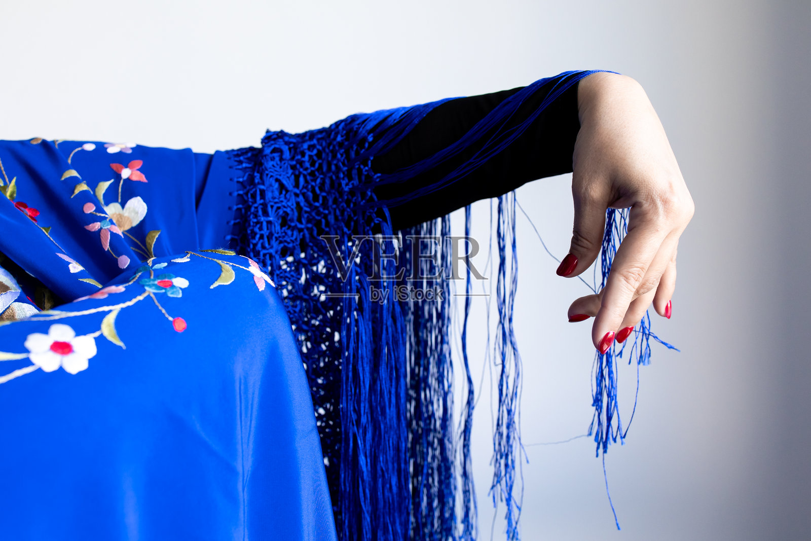 白人女性的手披着蓝色流苏披肩，上面有花卉刺绣。照片摄影图片
