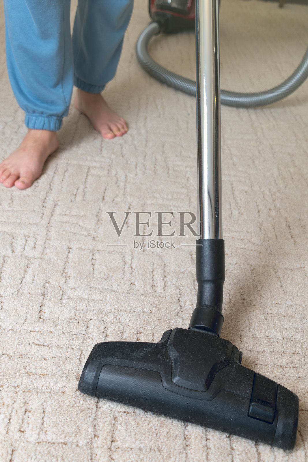一个赤脚的人在地毯上使用吸尘器清洁。照片摄影图片