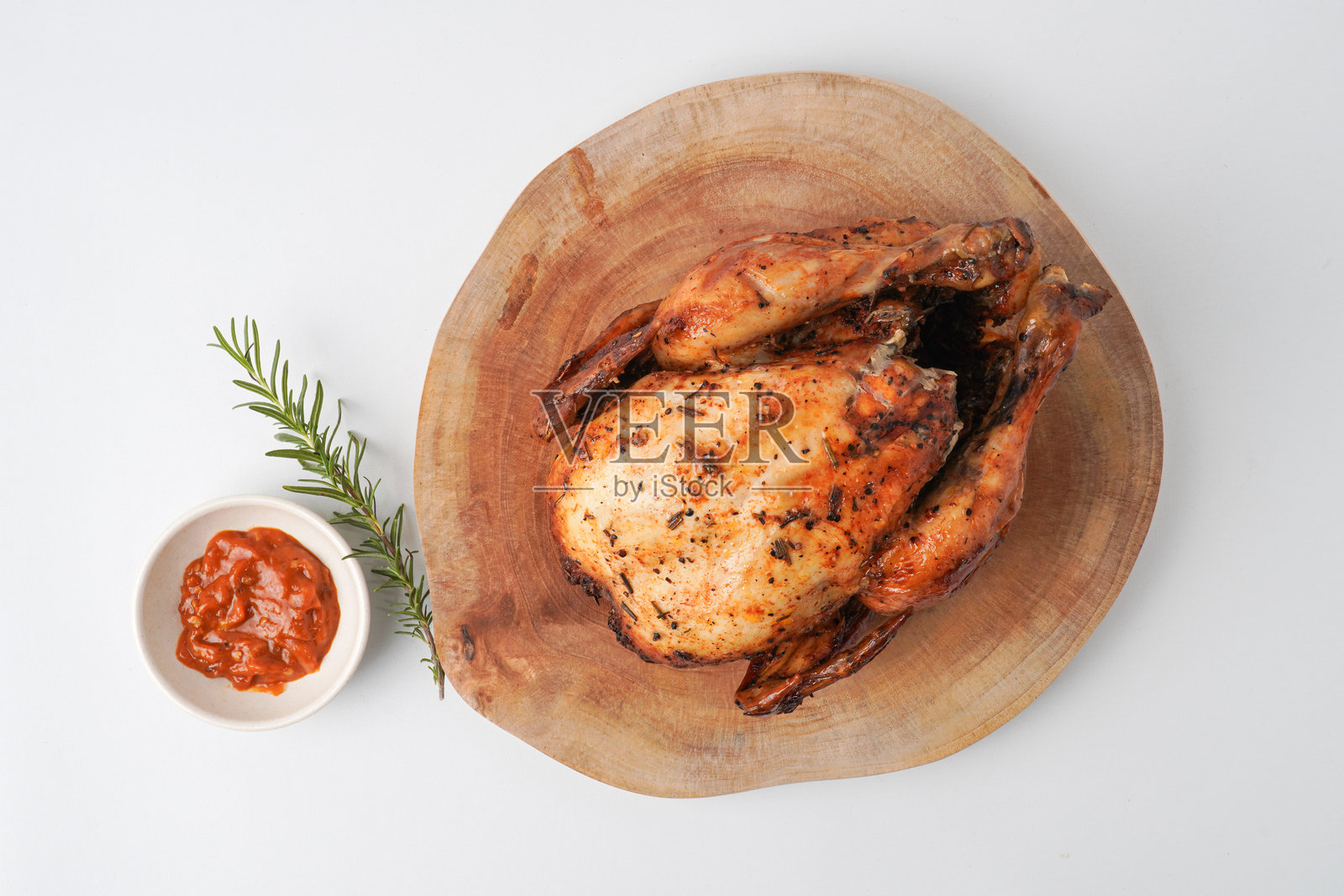 整只烤鸡放在木盘上，配有辣椒酱和迷迭香装饰。背景为白色。照片摄影图片