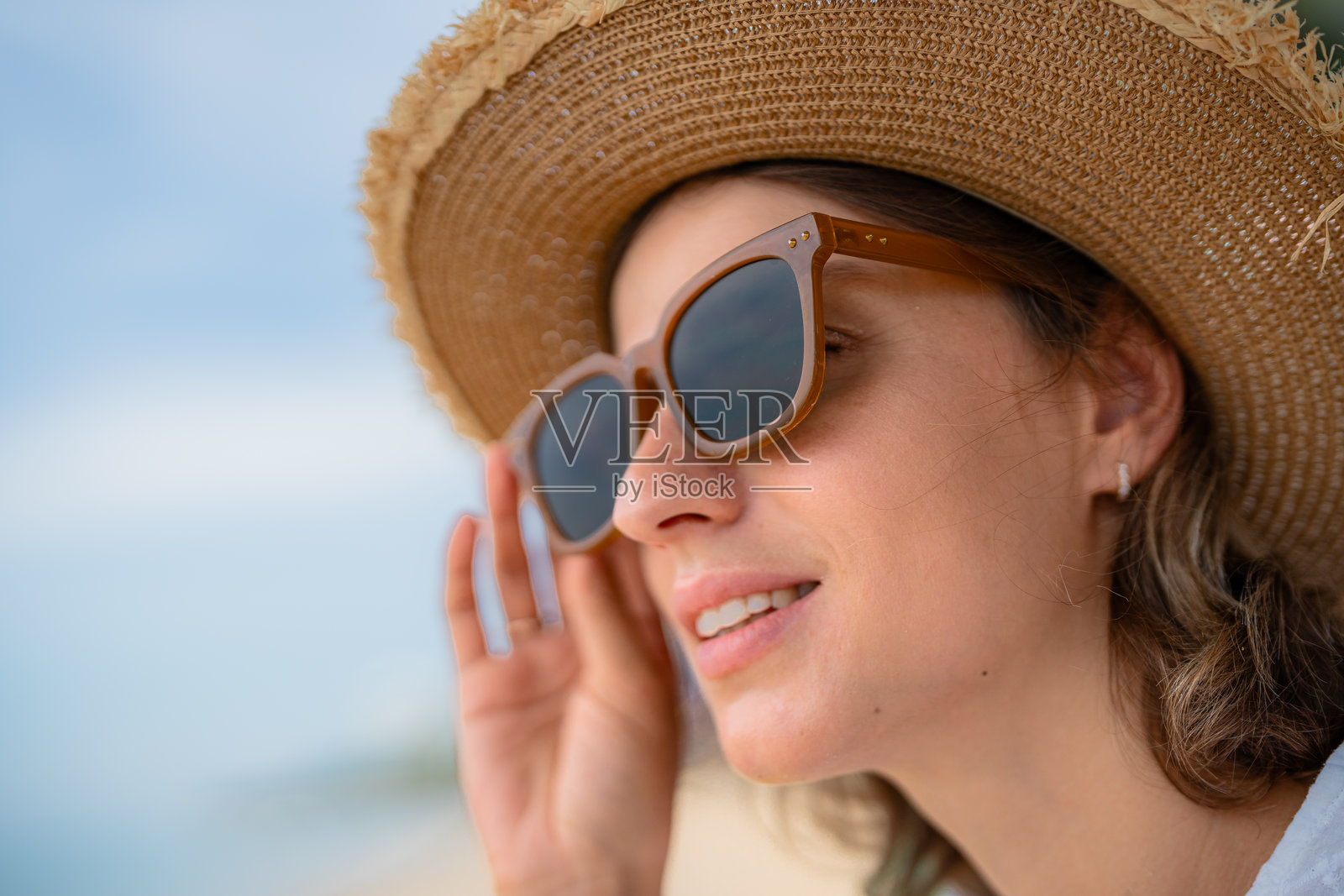 女人在阳光明媚的海滩上享受时光，戴着太阳镜和草帽。照片摄影图片