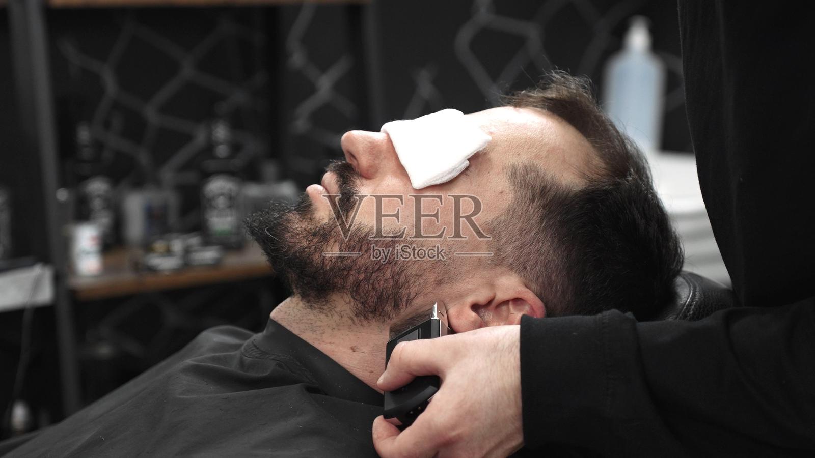 专业理发师在现代时尚的理发店环境中，熟练地使用电动剃须刀为顾客修剪胡须，确保造型精准且时尚。照片摄影图片