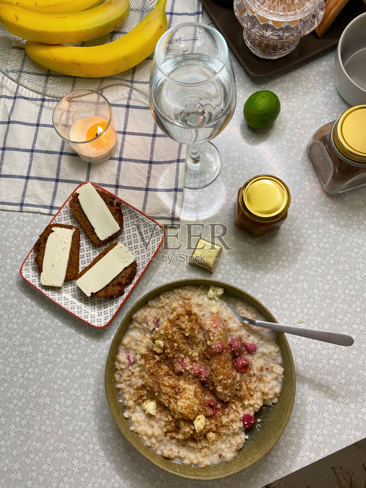 平铺的早餐，有燕麦粥和覆盆子。涂有黄油和青柠的香蕉面包片，蜡烛燃烧营造氛围。温馨的自制早餐。照片摄影图片