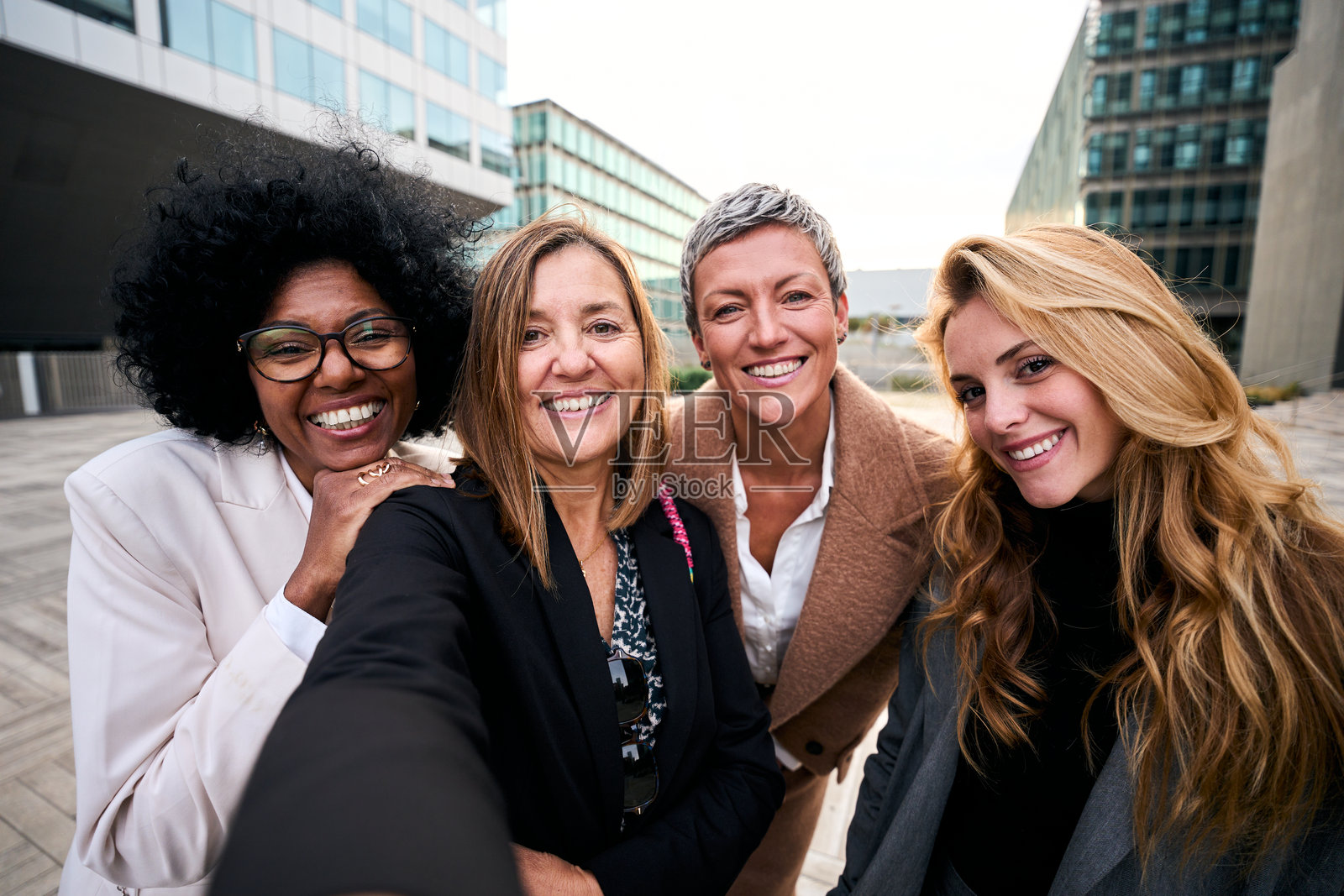 一群微笑的多种族女性商务人士穿着正式西装在户外自拍，面向镜头。照片摄影图片
