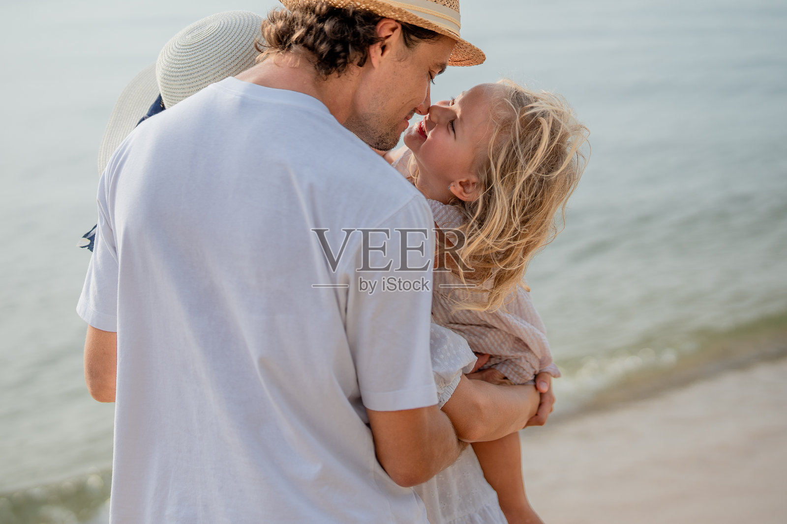 父亲和女儿在日落时分的海滩上分享快乐时光，拥抱着岸边的爱与温情。照片摄影图片