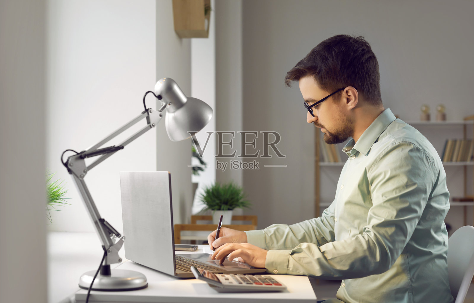 年轻严肃的商人在家中使用笔记本电脑工作并写作。照片摄影图片