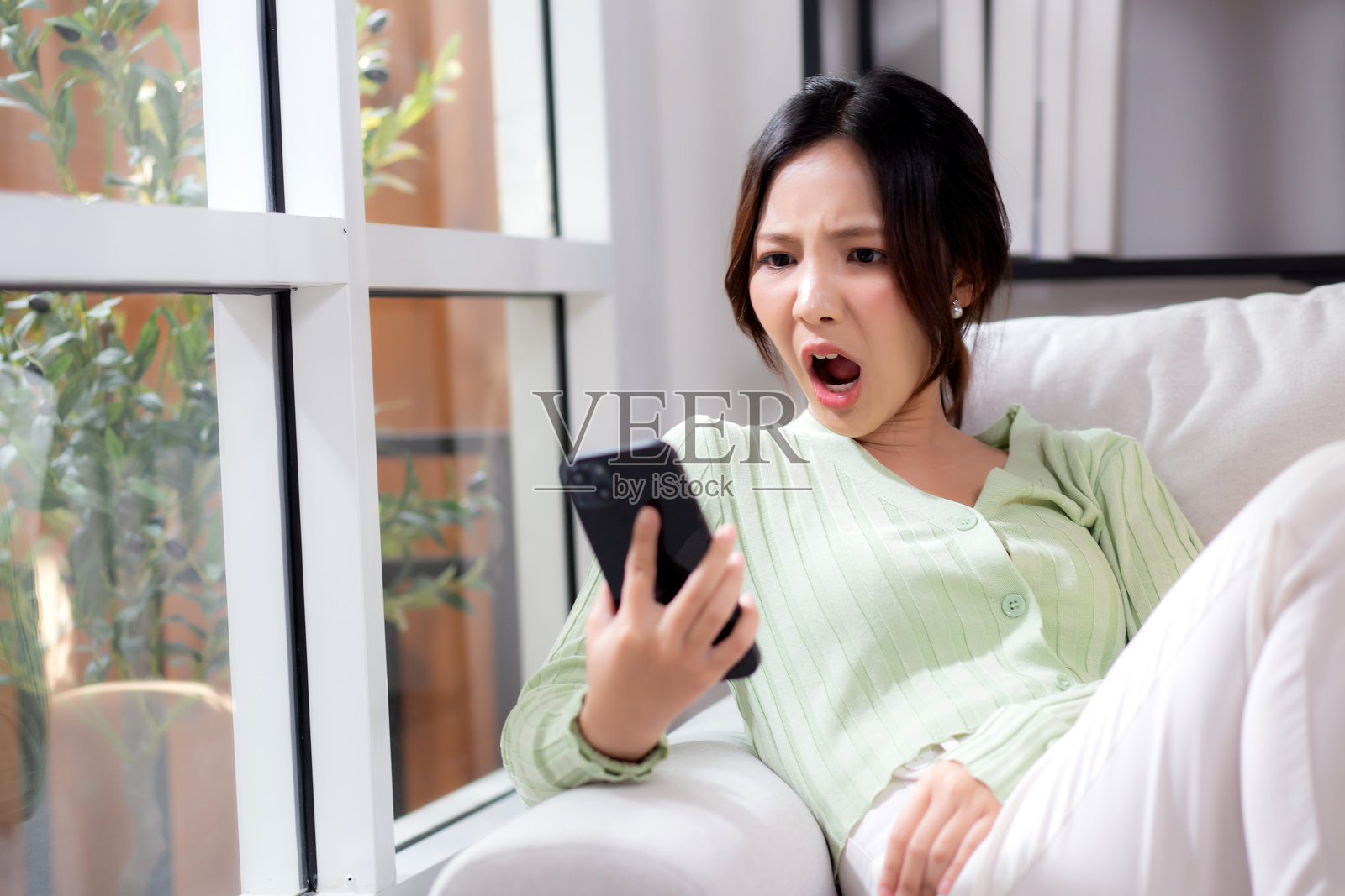 亚洲年轻女性坐在沙发上，神情紧张和担忧，正在家中的客厅里用智能手机通话，女性不快乐且关心地与手机通话，生活方式与沟通。照片摄影图片