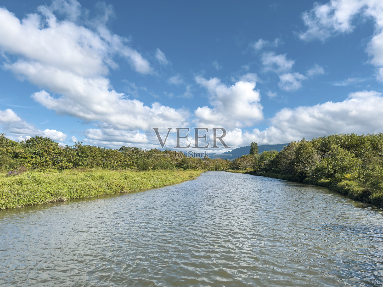 宁静的河流穿过绿色的风景，映衬着蓝天照片摄影图片