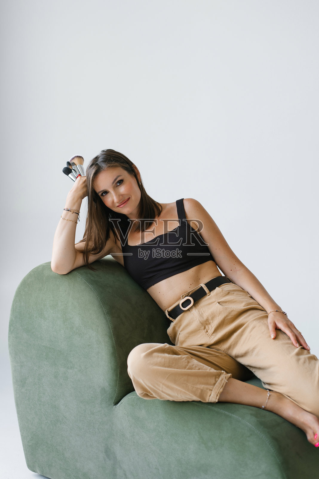 化妆师坐在绿色沙发上，手里拿着化妆刷，面带微笑。照片摄影图片