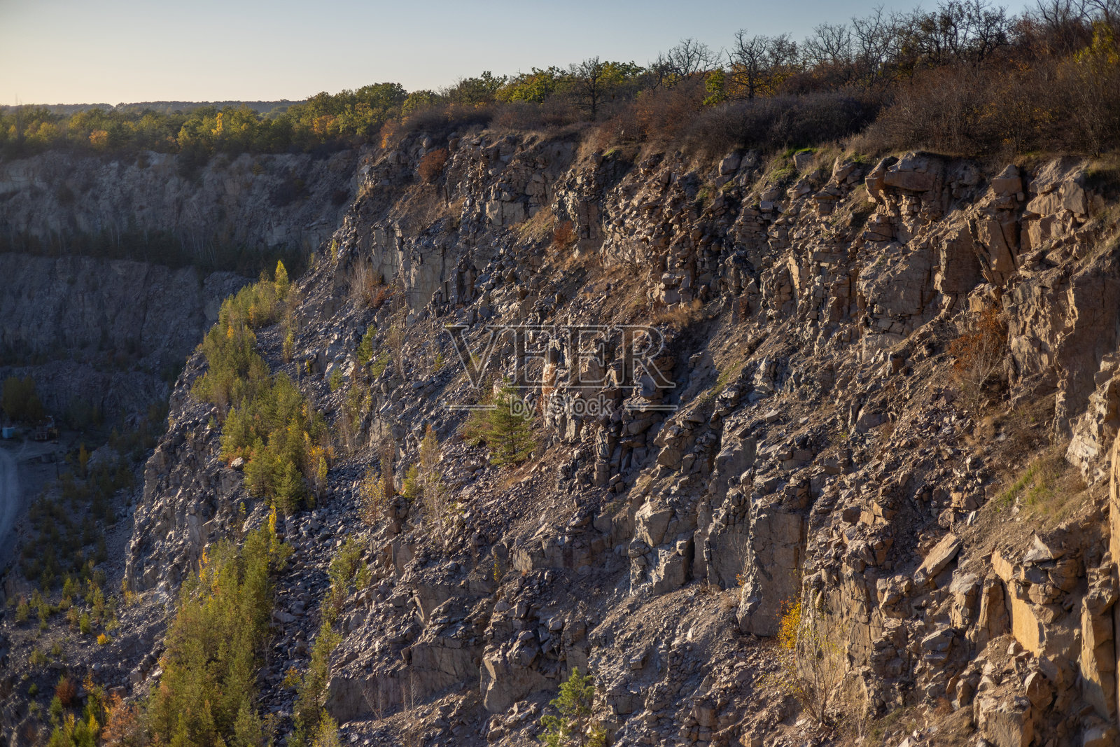 崎岖的悬崖，表面粗糙，沐浴在金色阳光下，稀疏的植被点缀其间。崎岖的地形突显了自然侵蚀的痕迹，干枯的植物散落其间，土色调主导着整个景观。照片摄影图片