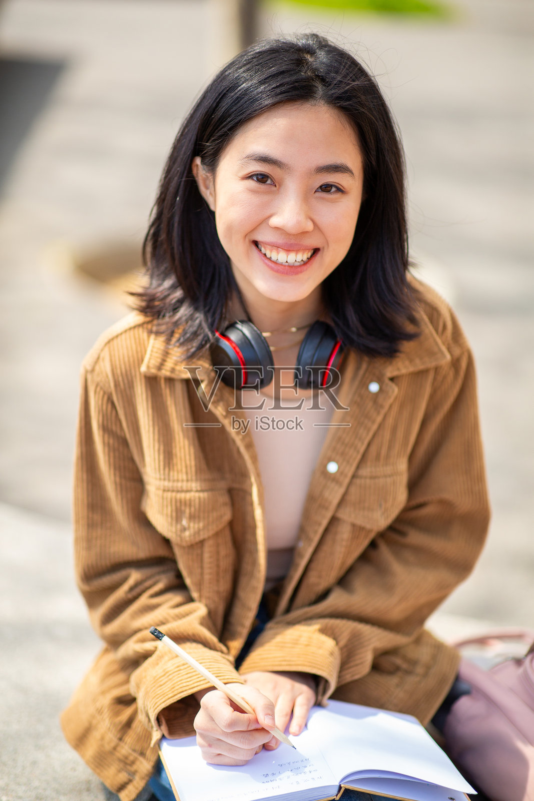 年轻女性坐在户外，手持笔和书籍照片摄影图片