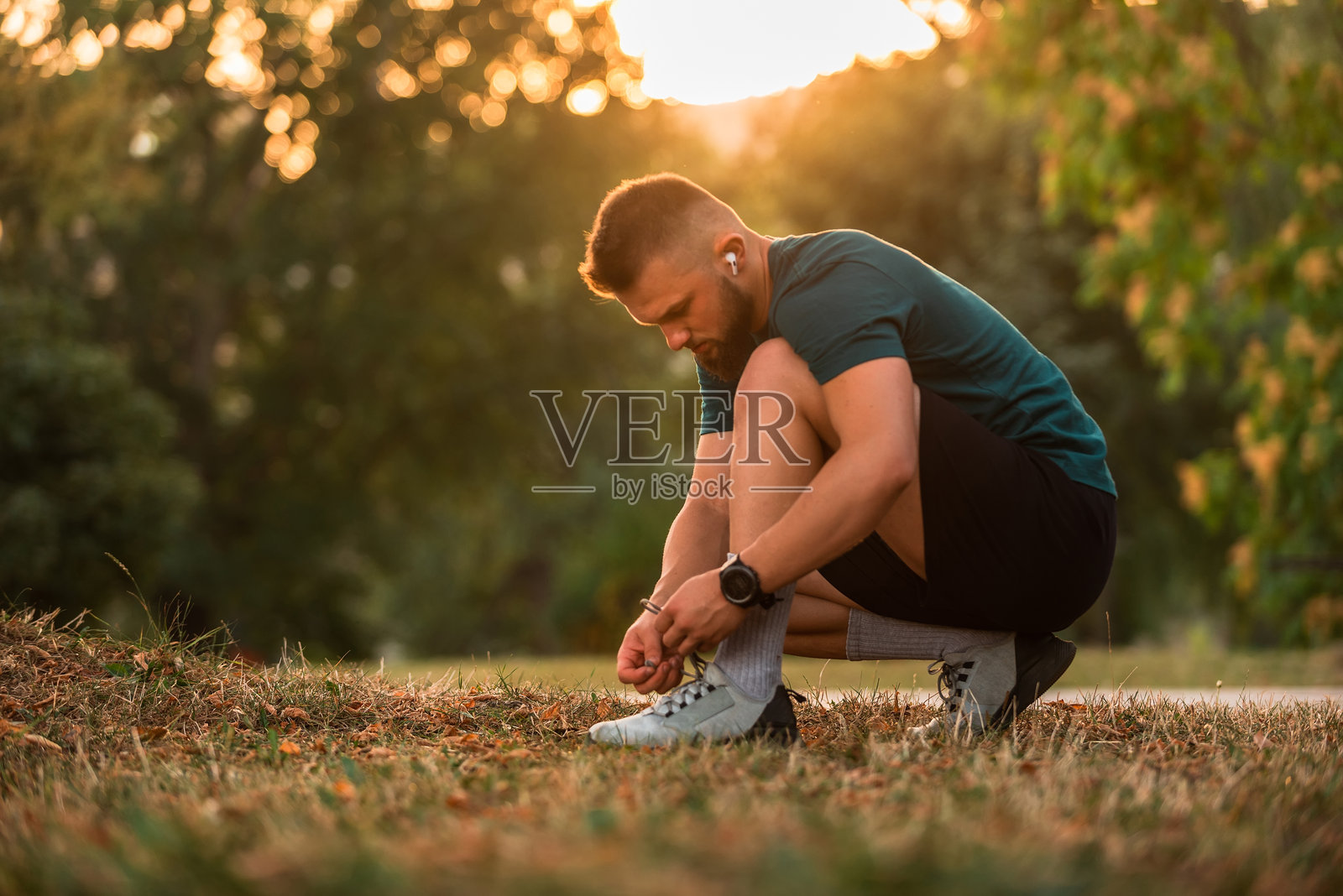 一位年轻的运动男士正在系跑鞋，佩戴无线耳机听音乐以激励自己，为在公园跑步或锻炼做准备，展现积极的生活方式。照片摄影图片