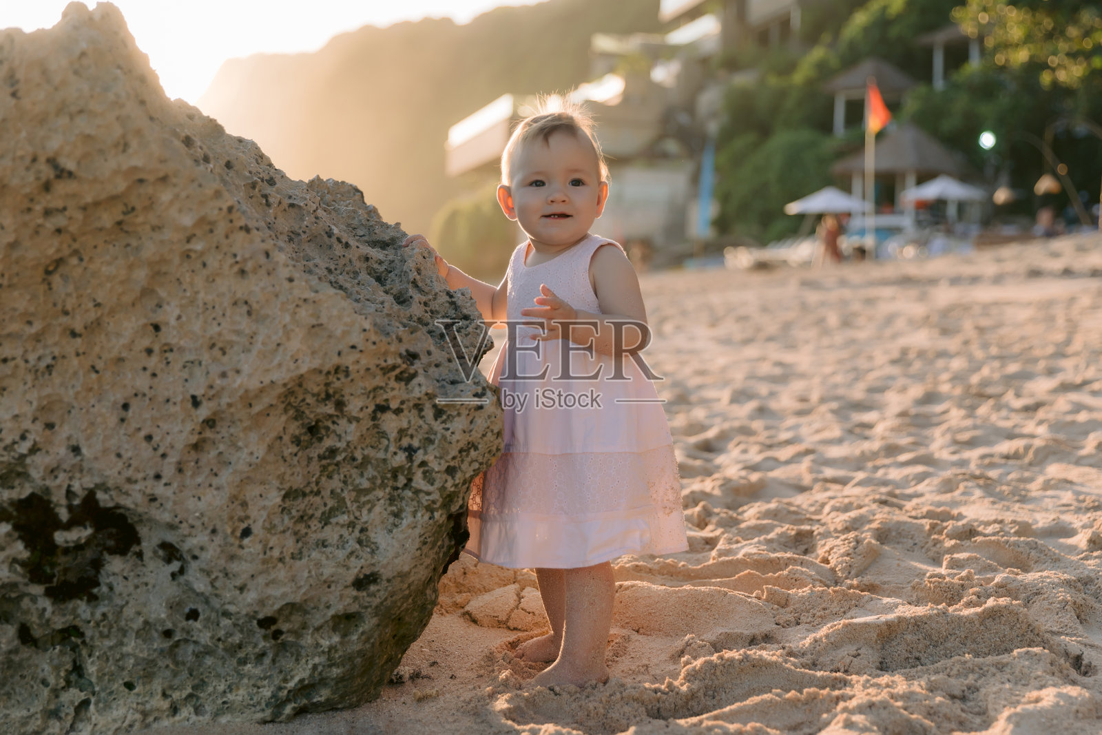 阳光下美丽的小女孩。穿着粉色裙子的孩子在日落海滩上。照片摄影图片