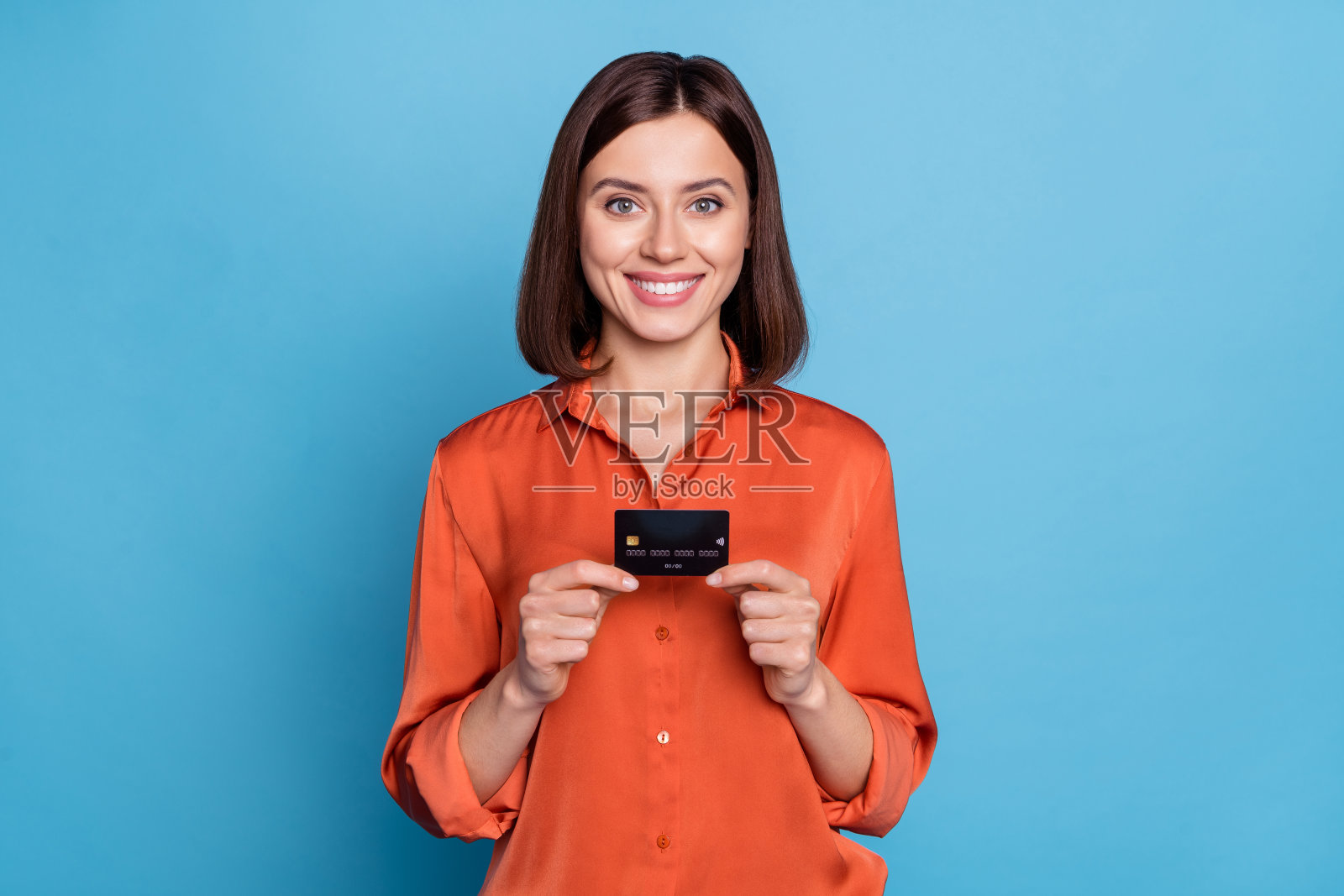 年轻漂亮的女性手持银行卡，展示收入福利薪水，背景为蓝色。照片摄影图片