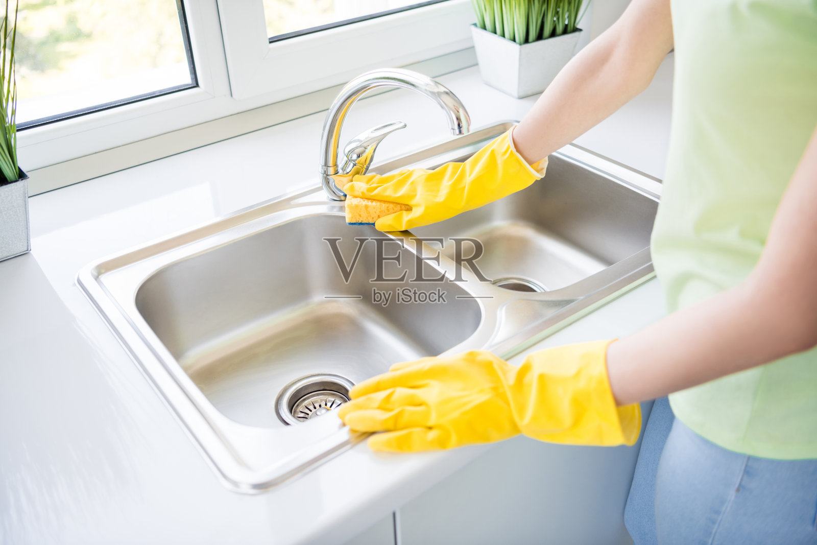 女士戴着橡胶手套用海绵擦拭厨房水槽的特写照片，阳光明媚的室内环境照片摄影图片