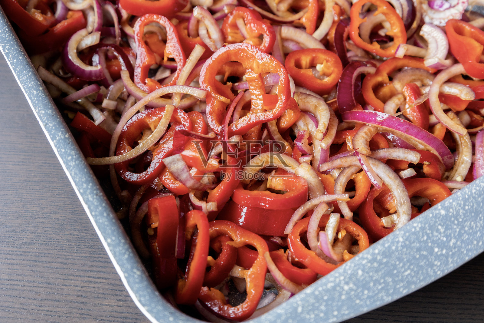 新鲜切片的红洋葱和红椒放在托盘中，调味后准备烘烤。这是一道色彩丰富、味道鲜美的蔬菜菜肴。照片摄影图片